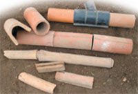 Figure 19.1 Drainage pipes. Modern clay pipes shown in the centre are butted up close together. An older method is shown below it and modern plastic piping is shown above. In the top left is a view of the modern clay pipe alongside the old ‘horse shoe’ tile (it would have sat on a ‘mug plate’ to prevent moving water washing away soil) and at the bottom are smaller examples of this type of old pipe
