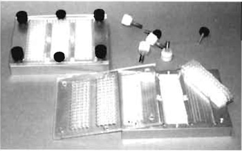 FIGURE 3 The arrayed slide is covered with a silicon rubber grid to give separate reaction chambers and is placed in a custom-made heat-conductive aluminium rack. A Plexiglas cover with a drilled hole through which the reaction chambers are accessed is tightly screwed on top the assembly, thus securing the silicon grid position during hybridisation.